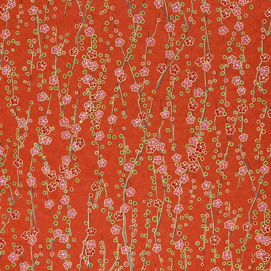 Japanese silk screen printed decorative chiyogami paper used on handmade cards. A patterned paper featuring delicate pink cherry blossom branches with small green leaves and dots on a warm orange-red background with hints of gold.