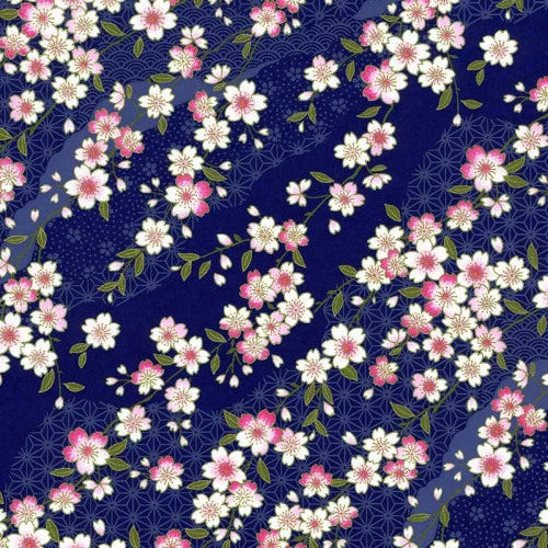 Japanese screen printed decorative chiyogami paper used in handmade cards. A repeating floral pattern featuring white and pink cherry blossoms with green leaves on a dark navy blue background with a subtle geometric wave design.